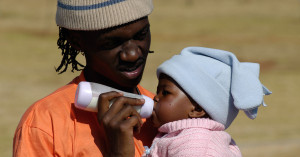 A fathers holds a baby, feeding the child with a bottle.
