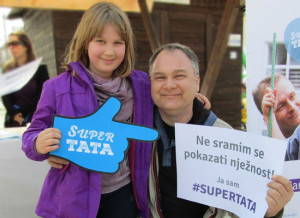 A father in Croatia holds a sign that reads: "I am not ashamed to show tenderness."