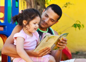 A father in Brazil reads a book to his daughter outside.