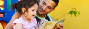 A father in Brazil reads a book to his daughter outside.