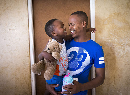 A smiling father holding his smiling son.