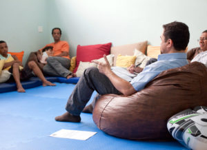 Men sit in a circle talking. One man is holding a child.