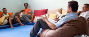 Men sit in a circle talking. One man is holding a child.