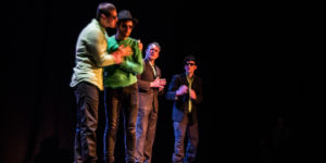 Four men on a stage, with one man embracing another.
