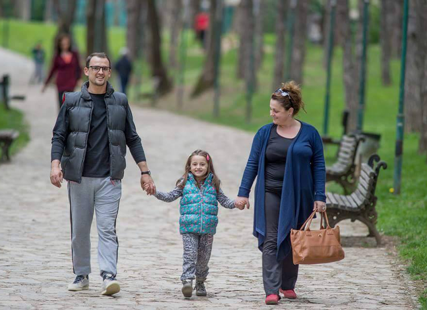 A man and a women walk outside on a path holding hands with their young daughter.