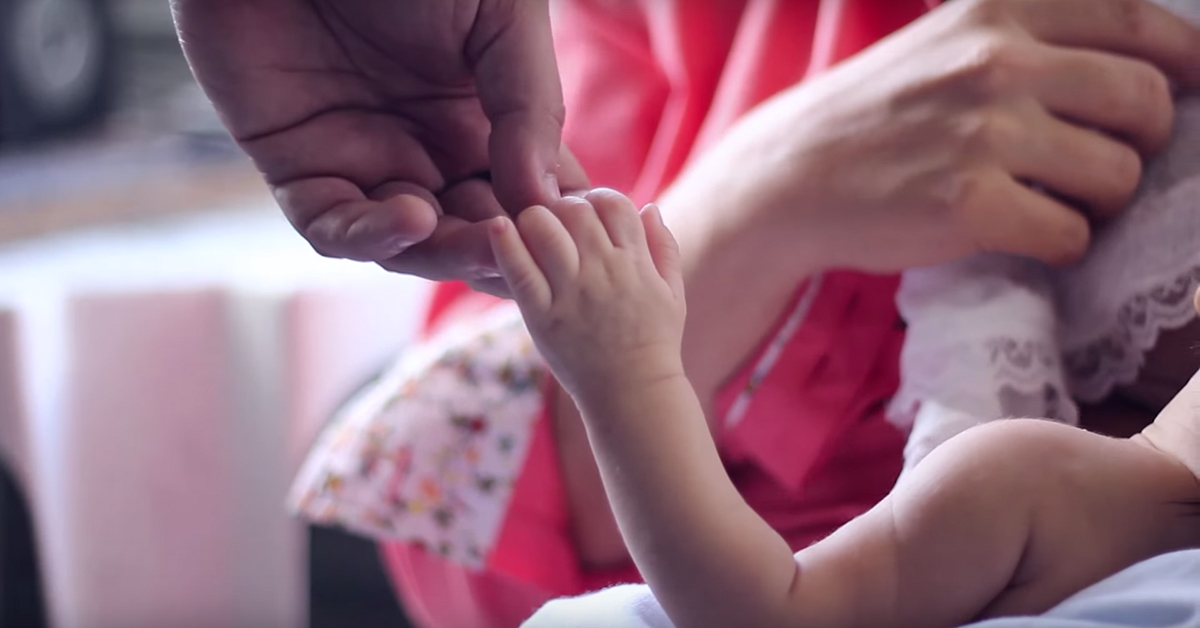 A father gently holds his newborn's hand in this still from the documentary "Pai não é visita! Pelo direito de ser acompanhante."