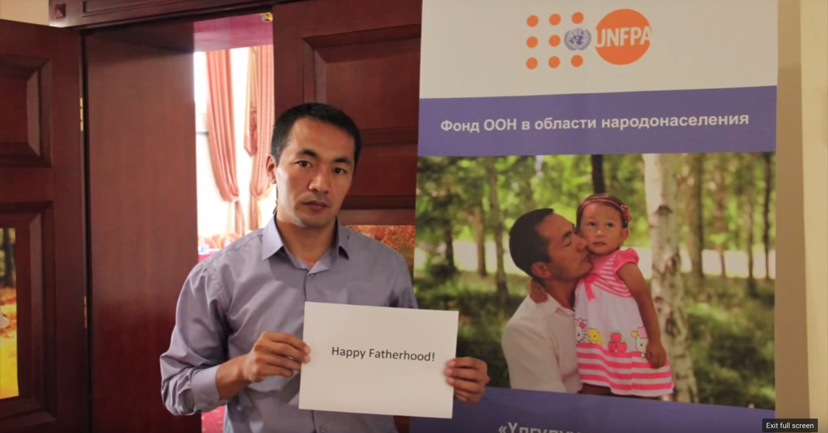 A man holds a sign that reads "Happy Fatherhood."