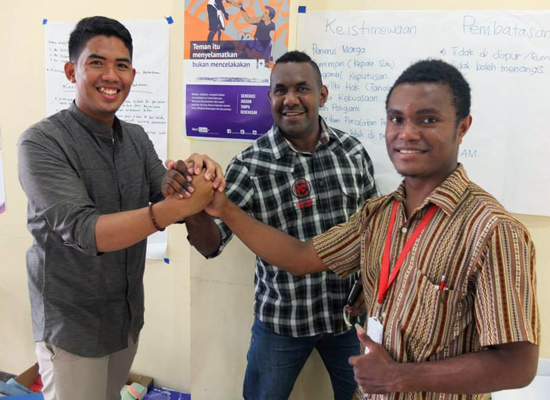 Three young men hold hands at a MenCare+ Indonesia facilitator training in Papua.