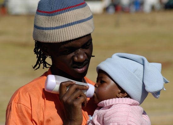 A fathers holds a baby, feeding the child with a bottle.