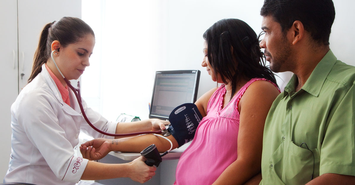 A health worker takes the blood pressure of a pregnant women who is accompanied by her partner.