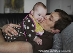 A father holds a baby. Photo: Johan Bävman / mencare.swiss.