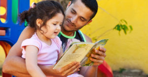 A father in Brazil reads a book to his daughter outside.