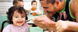 A smiling father feeds his laughing daughter.