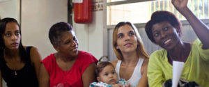 Four women (one holding a baby) sitting in a row.
