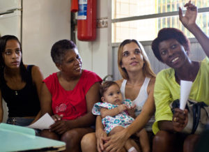 Four women (one holding a baby) sitting in a row.