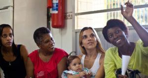 Four women (one holding a baby) sitting in a row.