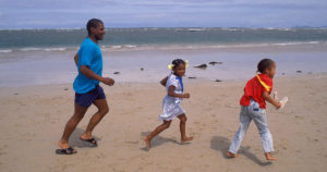 A man and two children run on the beach.
