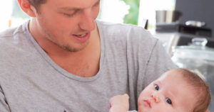Image of a man holding a baby, from the cover of "The MenCare Parental Leave Platform: Netherlands Platform."