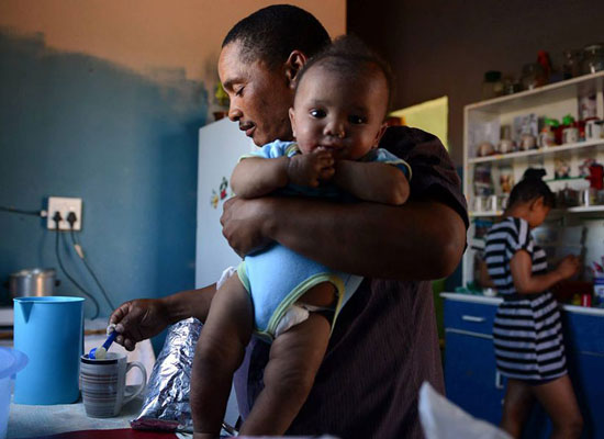 Man holding baby and cooking in South Africa.