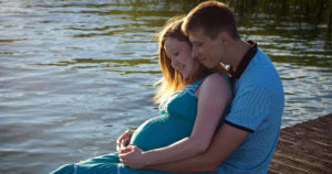 A man embraces his pregnant partner.