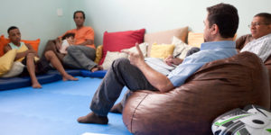 Men sit in a circle talking. One man is holding a child.