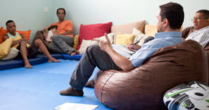 Men sit in a circle talking. One man is holding a child.